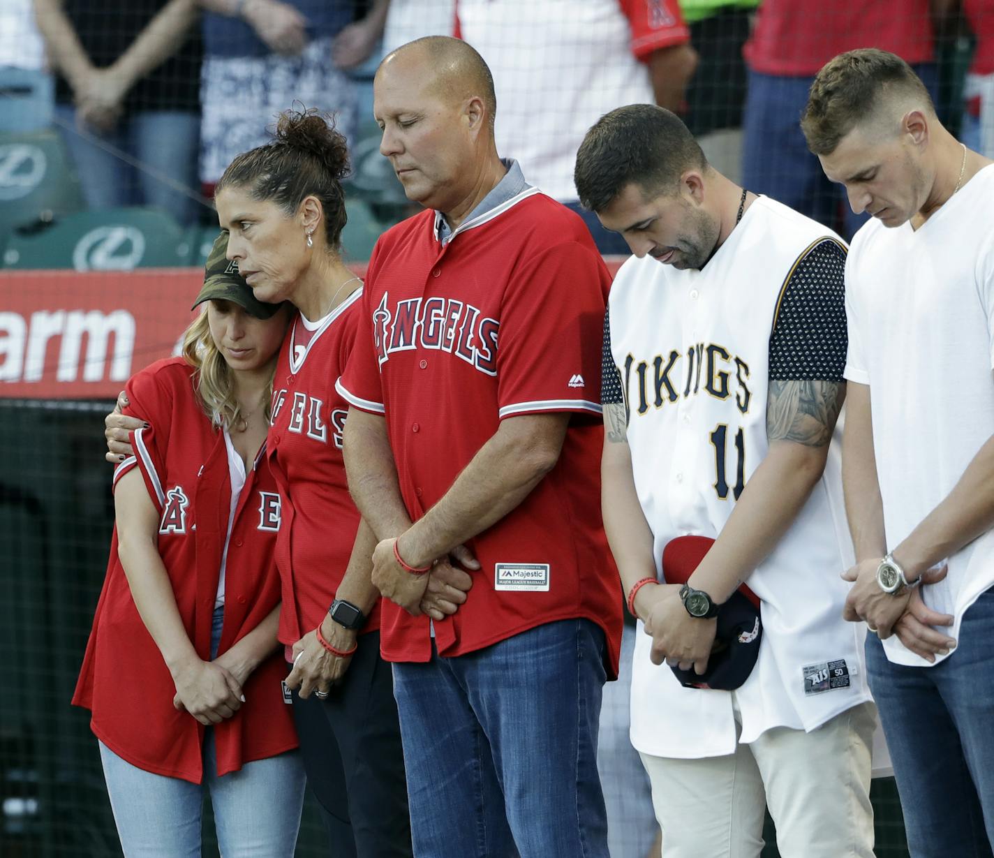 CORRECTS MOTHER'S LAST NAME TO HETMAN, INSTEAD OF SKAGGS - CORRECTS NAME OF PERSON AT MIDDLE - Members of Tyler Skaggs' family, including wife, Carli, left; mother, Debbie Hetman, second from left; and Danny Hetman, third from left, join in a moment of silence in Tyler's honor before the Los Angeles Angels' baseball game against the Seattle Mariners on Friday, July 12, 2019, in Anaheim, Calif. (AP Photo/Marcio Jose Sanchez)