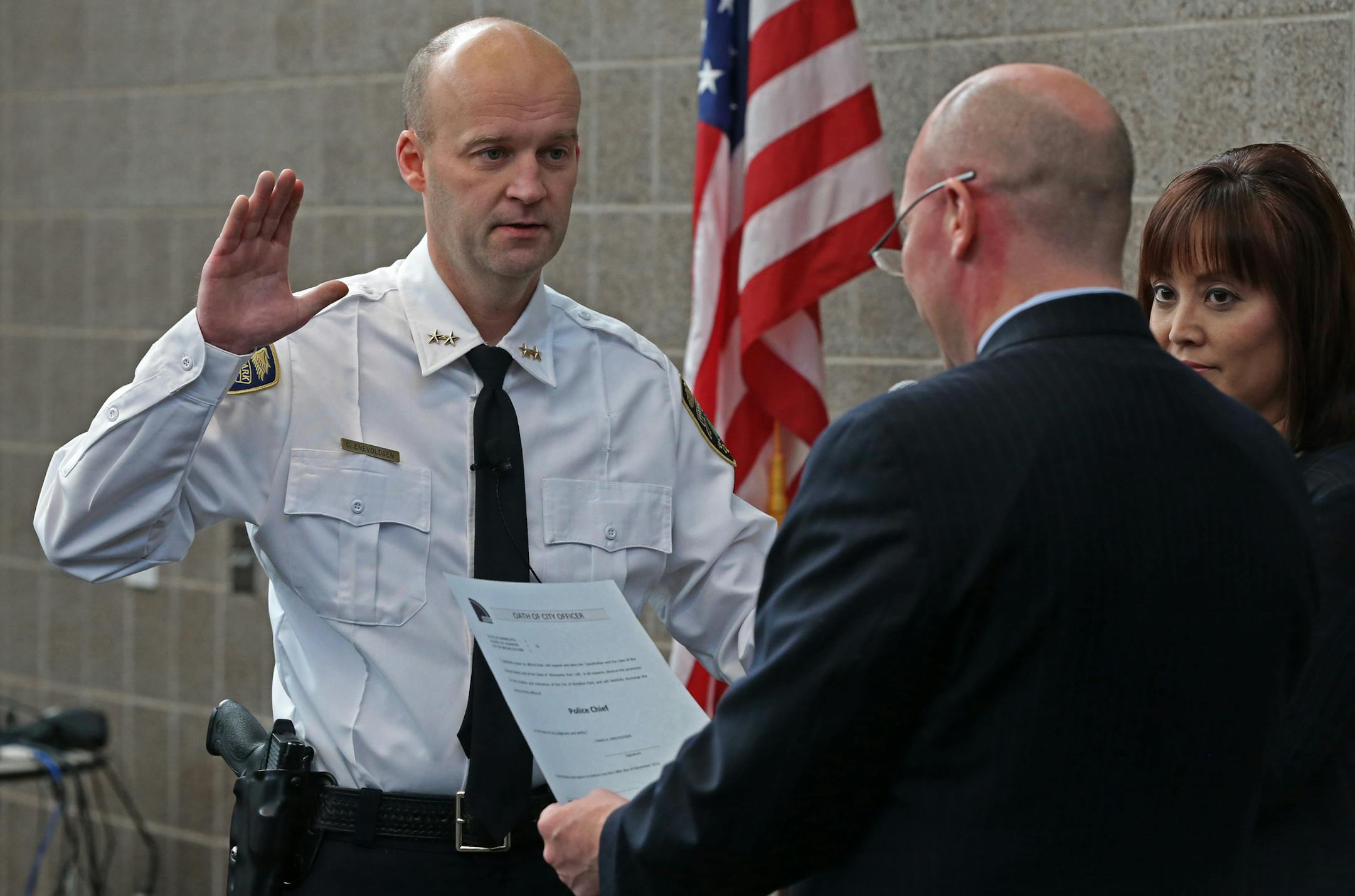 (left to right) New Brooklyn Park Police Chief Craig Enevoldsen, was sworn in by City Manager Jamie Verbrugge, as Mary Tan, Communications Coordinator, assisted, during ceremonies at the Brooklyn Park police headquarters on 12/17/13. Enevoldsen started as a city patrolman 22 years ago. Enevoldsen, 43, of Buffalo, has served as acting chief since Mike Davis left to become Public Safety head at a Boston area college. The city did an internal search and Craig was the only applicant.] Bruce Bisping/