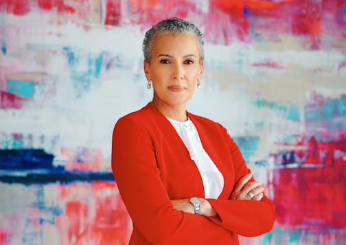 A woman in a red blazer is photographed in front of a modern art canvas.