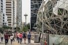 With the Space Needle observation tower visible in the distance, pedestrians walk past a recently built trio of geodesic domes that are part of the Se