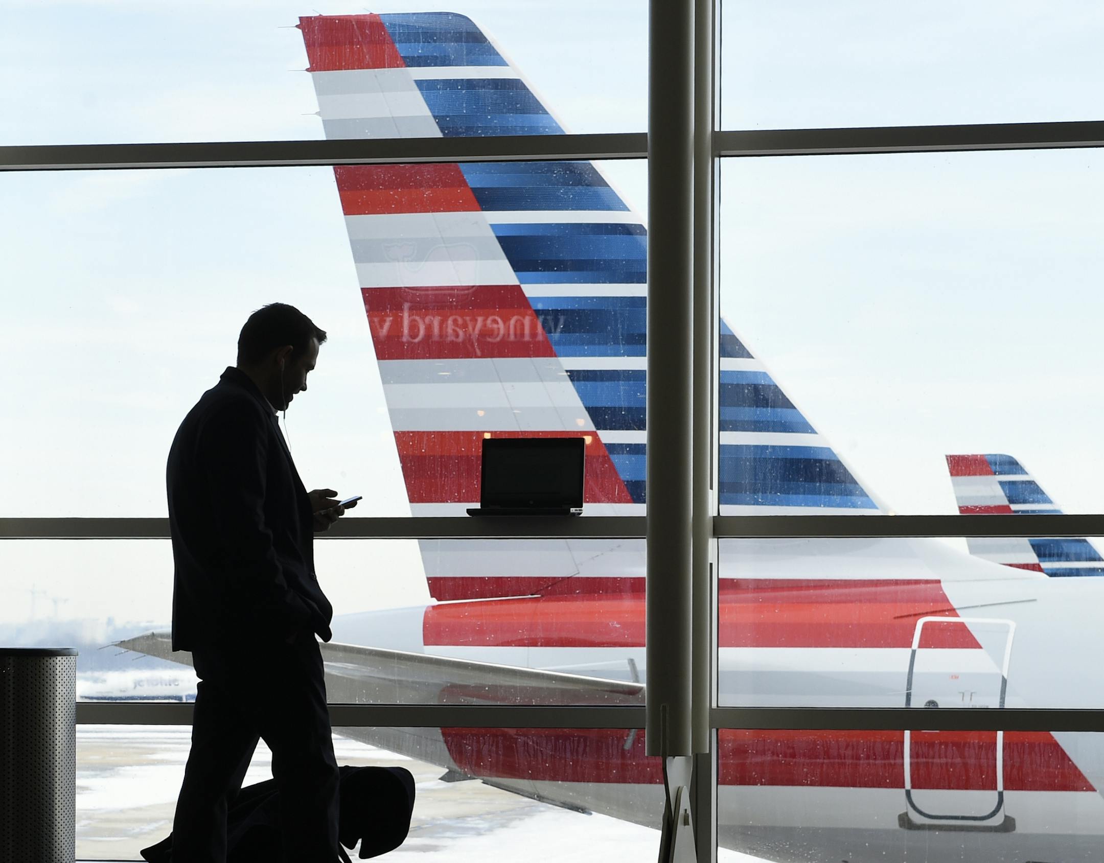 FILE - In this Jan. 25, 2016, file photo, a passenger talks on the phone as American Airlines jets sit parked at their gates at Washington's Ronald Reagan National Airport. After 15 years of cutbacks, U.S. airlines are starting to add back some small perks for everyday coach passengers. On Monday, Feb. 1, American became the latest carrier to add something back, announcing the return of free snacks in the economy section and more free entertainment options on some aircraft. (AP Photo/Susan Walsh