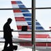 FILE - In this Jan. 25, 2016, file photo, a passenger talks on the phone as American Airlines jets sit parked at their gates at Washington's Ronald Re