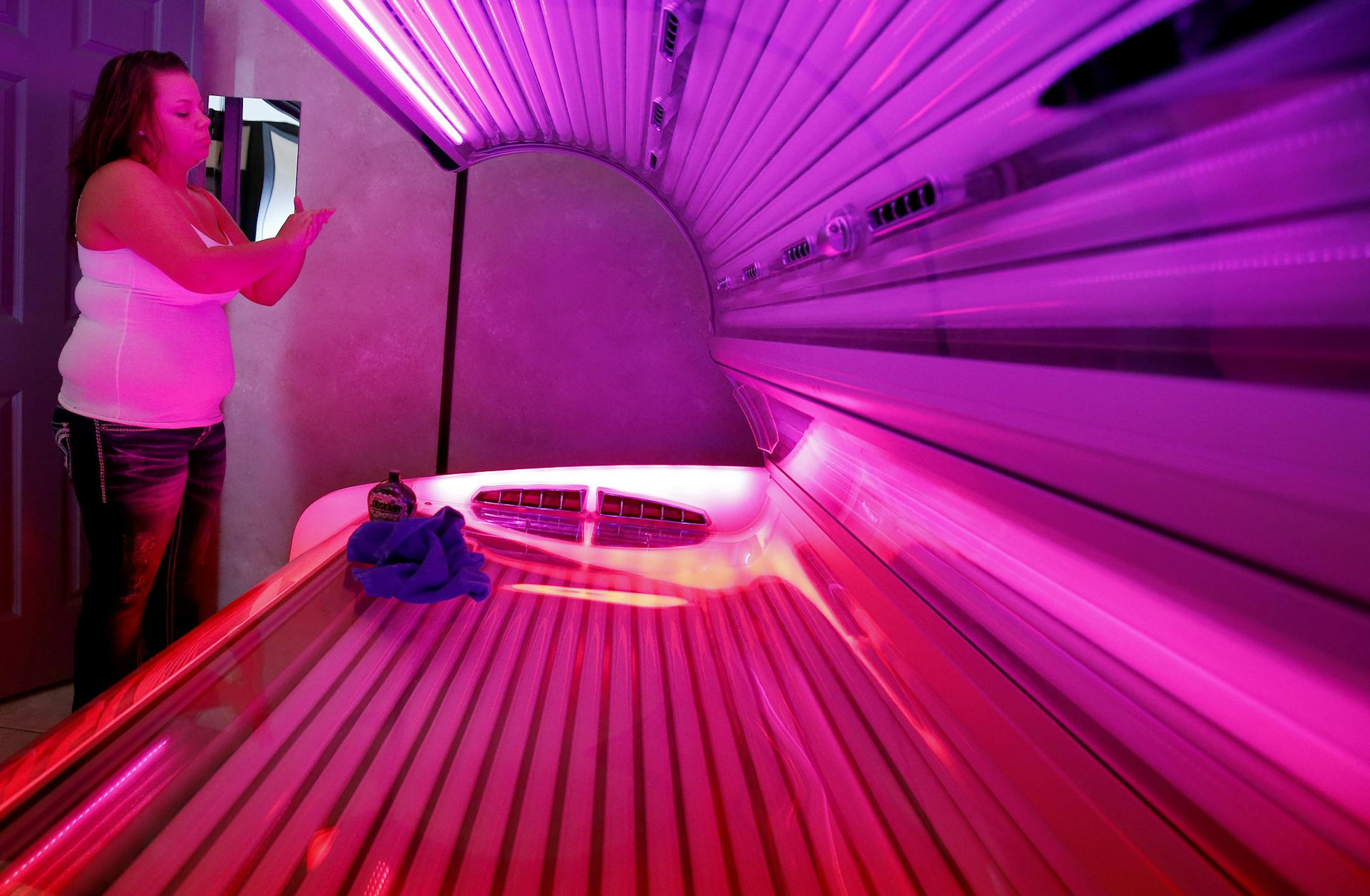 Ashley Blanshan, 22, of Blaine applied a bronzing lotion as she prepared to tan at Totally Tan in Golden Valley on Wednesday. Blanshan said she tans twice a week during the winter. ] CARLOS GONZALEZ cgonzalez@startribune.com - March 26, 2014 , Golden Valley, Minn., Totally Tan, A bill authored by Sen. Chris Eaton (DFL-Brooklyn Center) that would establish an age limit on the use of tanning equipment was recently sent to the Senate floor. S.F. 1901 would prohibit minors from using indoor tanning