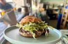 The Pão burger on the bar at Hola Arepa, topped with shreds of lettuce and just a little bit of mayo. The bun is threaded with rivers of melted chees