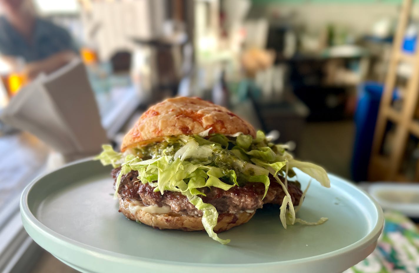 The Pão burger on the bar at Hola Arepa, topped with shreds of lettuce and just a little bit of mayo. The bun is threaded with rivers of melted cheese.