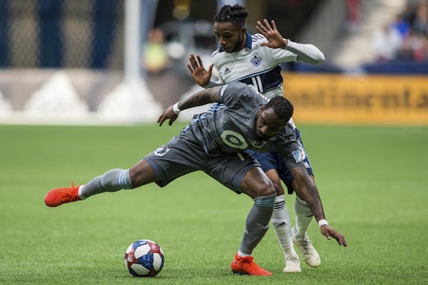 Vancouver Whitecaps' Alhassane Bangoura, rear, plays the ball against Minnesota United's Romain Metanire during the second half of an MLS soccer match