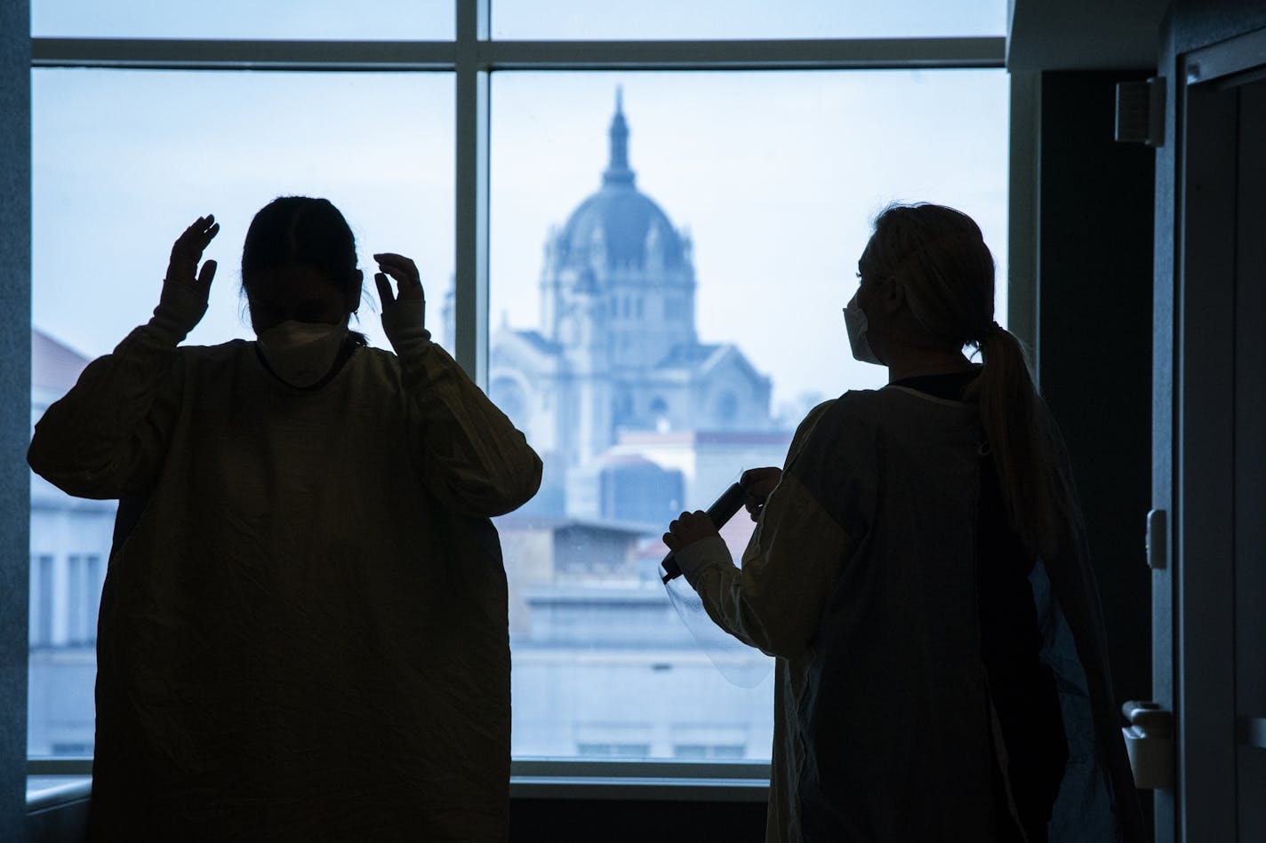 Susan Ehman, left, RN, and Bethany Webb, RN, don PPE to go into a COVID-19 patient's room in the ICU at Regions Hospital in St. Paul. The Cathedral of St. Paul is seen in the background.