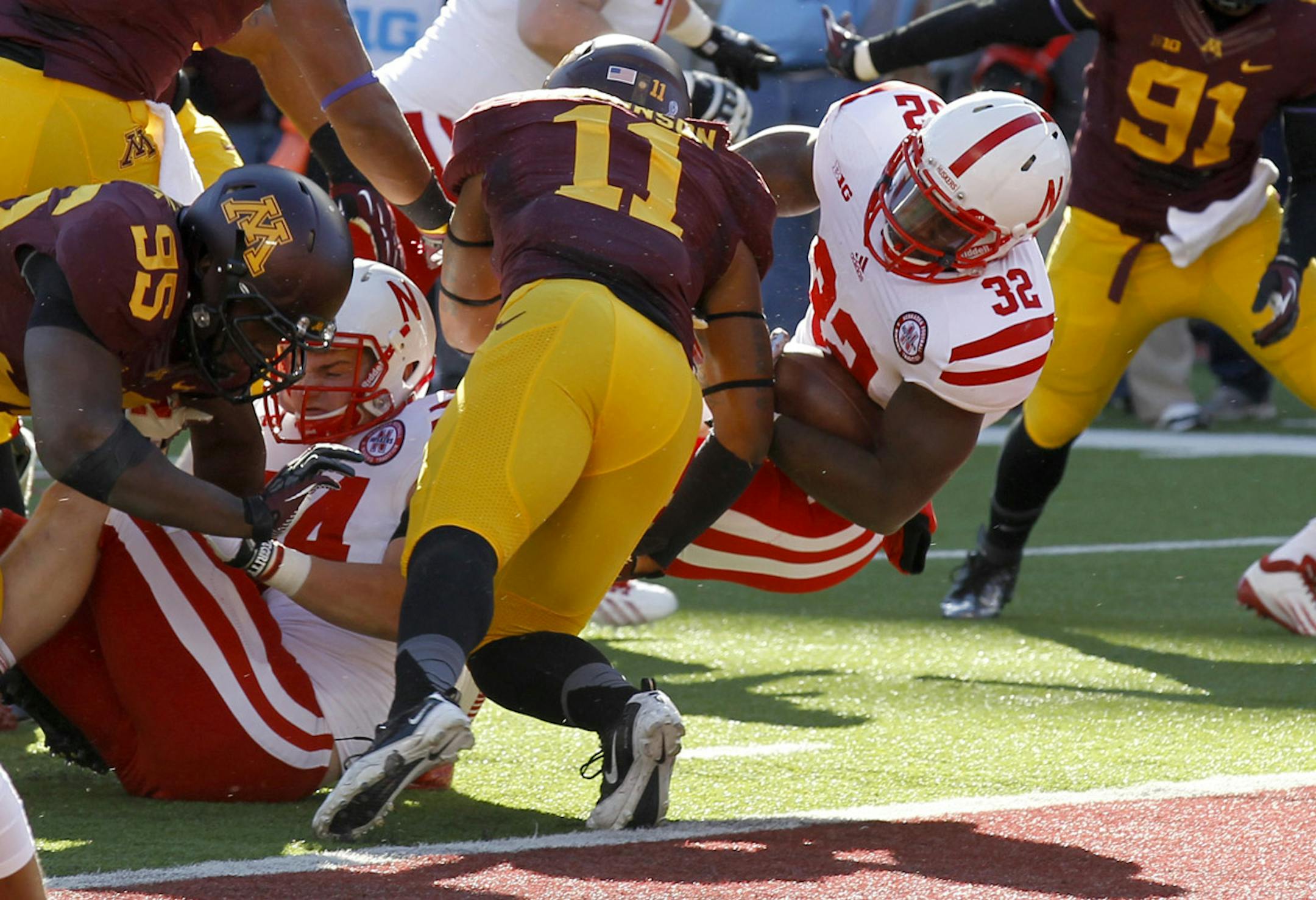 Nebraska running back Imani Cross (32) falls into the endzone past Minnesota defensive back Antonio Johnson (11) for a touchdown during the first quarter of an NCAA college football game in Minneapolis Saturday, Oct. 26, 2013. (AP Photo/Ann Heisenfelt)