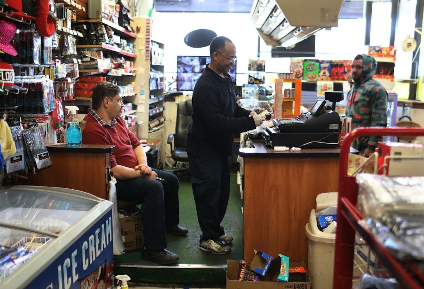 Phoenix Market manager Tarig Mohamed, center, makes change for a customer, as friend and customer Mustafa Naffa, left, looks on at the Dayton's Bluff neighborhood market Friday, March 20, 2020 in St. Paul, MN.