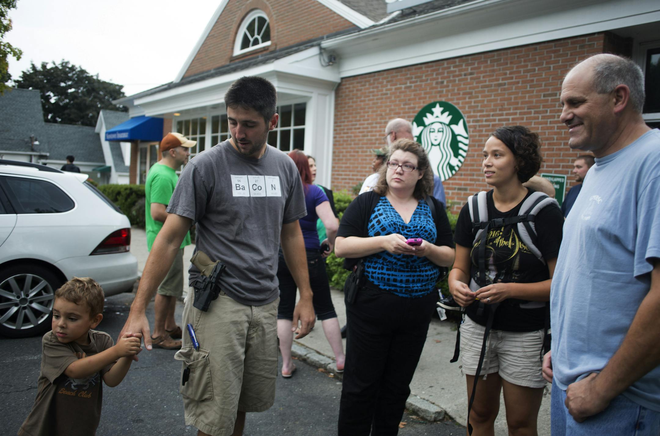 FILE -- Open carry supporters gather outside a Starbucks that closed early in response to their planned event in Newtown, Conn., Aug. 9, 2013. Starbucks, reversing a policy that had allowed customers to openly carry guns in states that allow it, said Sept. 18, 2013, that will now ask customers not bring firearms into its stores. The company said the policy was not a response to last year's shooting spree at Sandy Hook Elementary School in Newtown. (Lisa Wiltse/The New York Times)