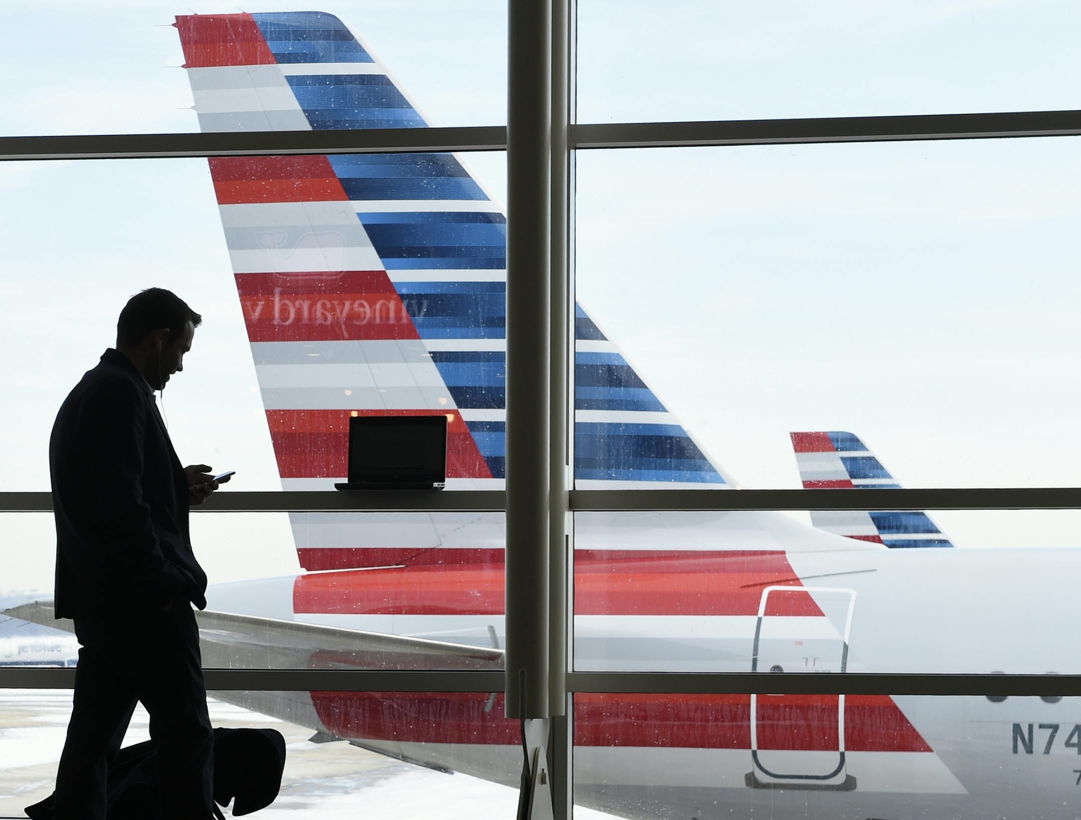 FILE - In this Jan. 25, 2016, file photo, a passenger talks on the phone as American Airlines jets sit parked at their gates at Washington's Ronald Reagan National Airport. After 15 years of cutbacks, U.S. airlines are starting to add back some small perks for everyday coach passengers. On Monday, Feb. 1, American became the latest carrier to add something back, announcing the return of free snacks in the economy section and more free entertainment options on some aircraft. (AP Photo/Susan Walsh