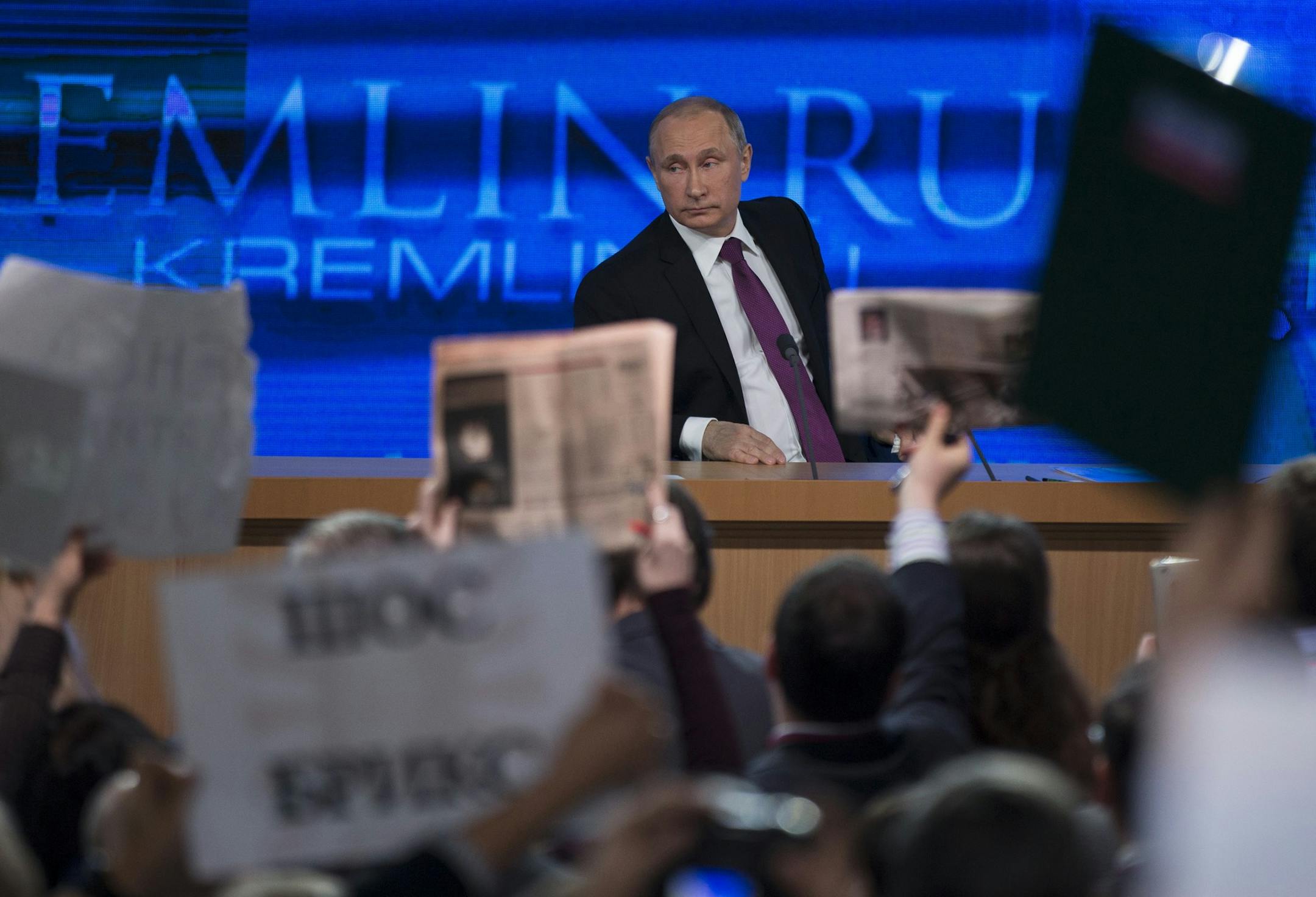 Journalists raise hands and posters and papers to attract attention, as Russian President Vladimir Putin, background, listens to a question, during his annual news conference in Moscow, Russia, Thursday, Dec. 18, 2014. The Russian economy will rebound and the ruble will stabilize, Russian President Vladimir Putin said Thursday at his annual press conference, he also said Ukraine must remain one political entity, voicing hope that the crisis could be solved through peace talks. (AP Photo/Pavel Go