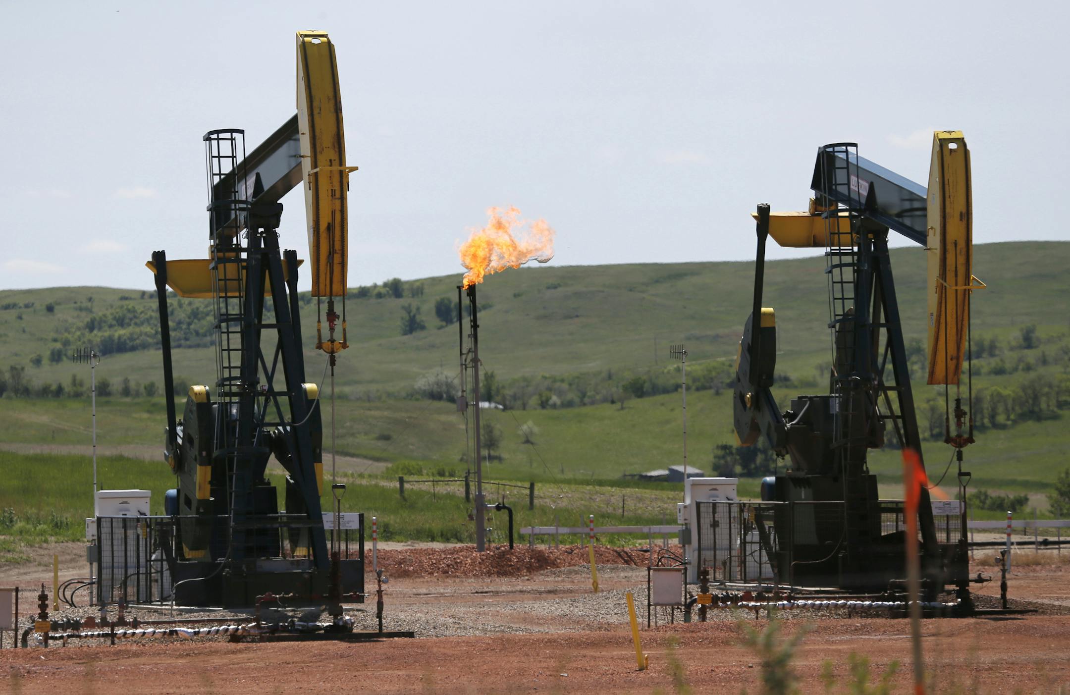 FILE -In this June 12, 2014 file photo, oil pumps and natural gas burn off in Watford City, N.D. Methane emissions will likely be the next big environmental issue to face North Dakota's booming oil industry according to a top official at the state's Department of Health. The Obama administration is finalizing a rule to cut methane emissions from U.S. oil and gas production by nearly half over the next decade. Itís part of an ongoing push by the president to curb climate change. (AP Photo/Ch