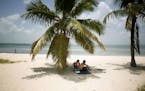 FILE - In this July 1, 2015 file photo, Marvin Hernandez, right, and Kelly Vera sit in the shade of a palm tree, in Key Biscayne, Fla. Florida's iconi