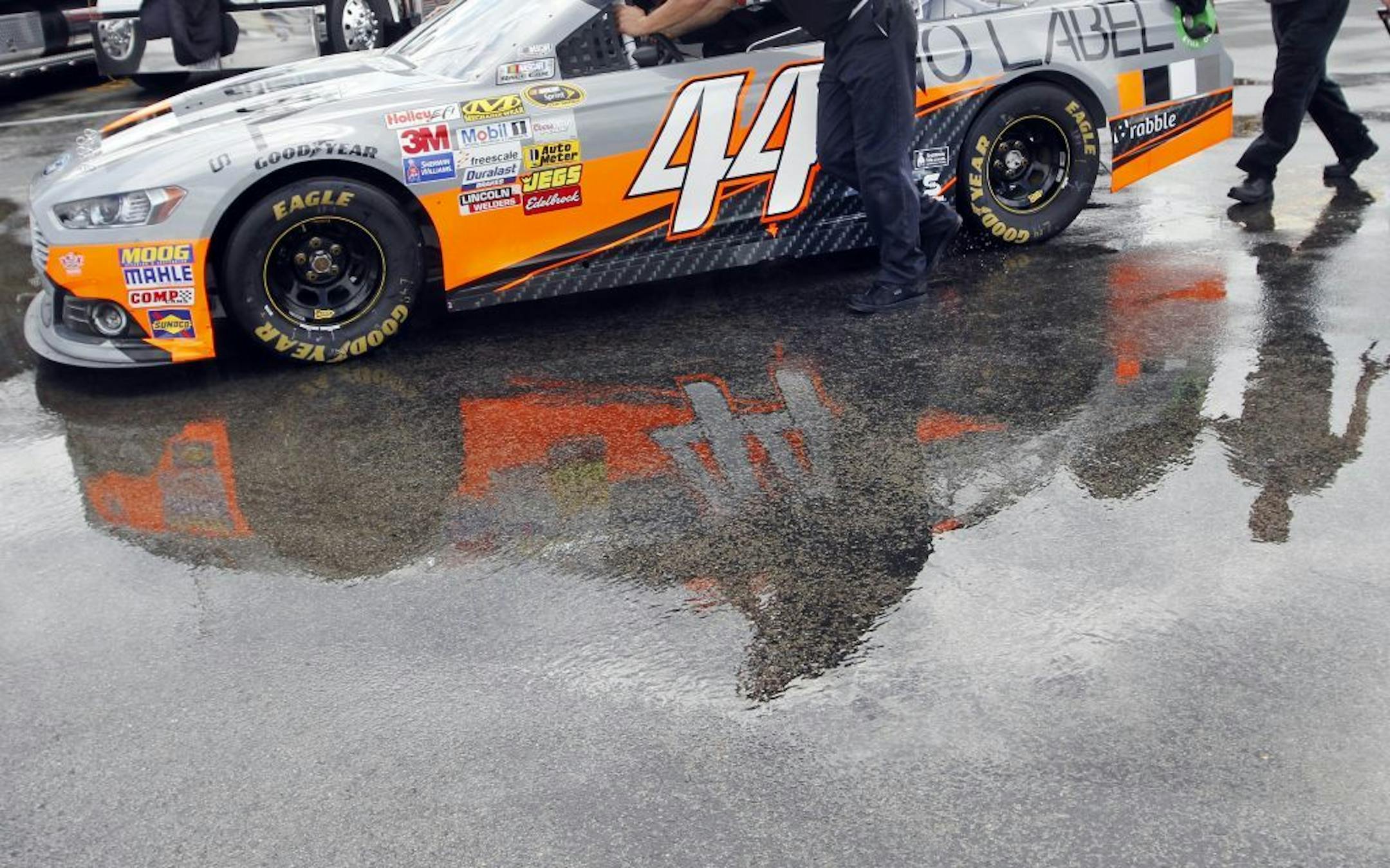 Crew members for Scott Riggs push his car through puddles between stations during tech inspection for the NASCAR Sprint Cup auto race at Kentucky Speedway in Sparta, Ky., Saturday, June 29, 2013.