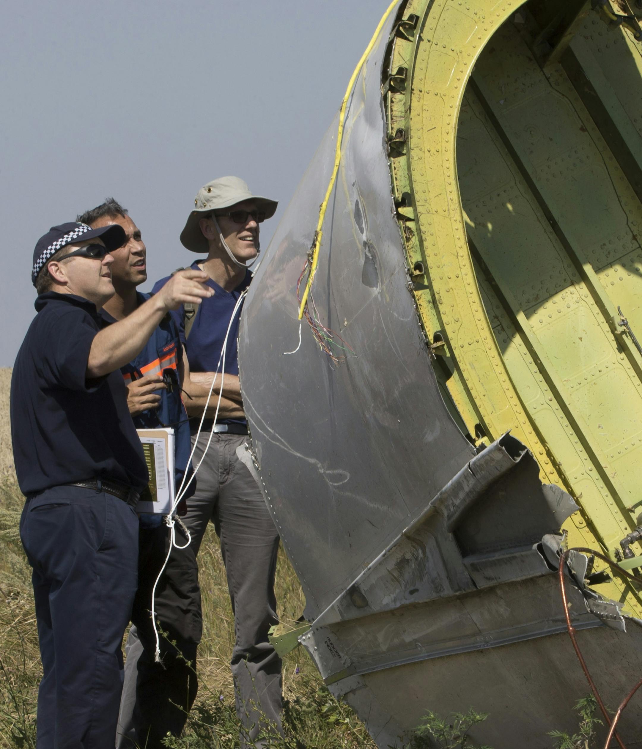 Australian and Dutch experts examine a piece of the Malaysia Airlines Flight 17 plane, near the village of Hrabove, Donetsk region, eastern Ukraine Friday, Aug.1, 2014. The investigators from the Netherlands and Australia plus officials with the Organization for Security and Cooperation in Europe traveled from the rebel-held city of Donetsk in 15 cars and a bus to the crash site outside the village of Hrabove. Then they started setting up a base to work from at a chicken farm. The investigative