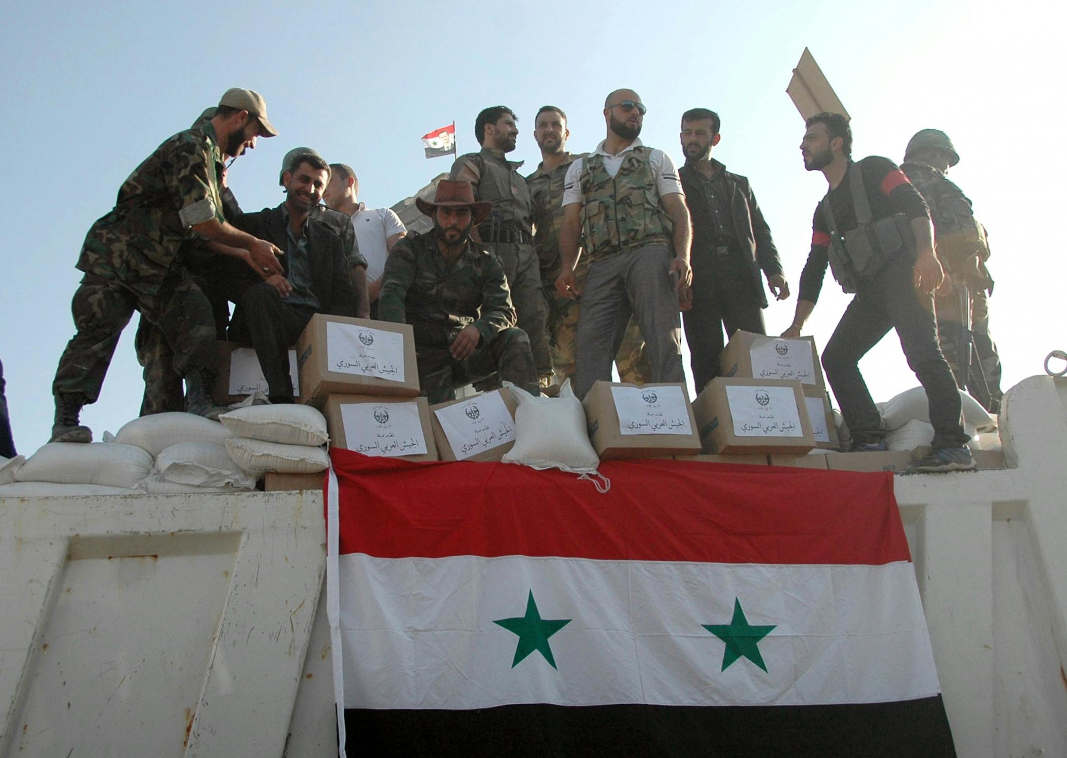 In this photo released on June 5, 2013 by the Syrian official news agency SANA, Syrian soldiers loyal to President Bashar Assad stand on a truck full of a aid supplies, in Qusair, Syria.