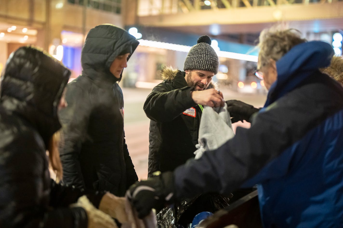 Steve Barnier hands Shawn Tierney a handmade hat as he and a few others hand our food and warm clothes to people passing by a bus stop in downtown Minneapolis, Minn, on Friday night, Feb. 3, 2023. Friday nights churchgoers and Bethel University students gather at ICCM Inner City Church before splitting into groups to drive out to homeless camps and public transport to give out hot food, blankets, and offer prayers to those wanting it. ] RENEE JONES SCHNEIDER • renee.jones@startribune.com