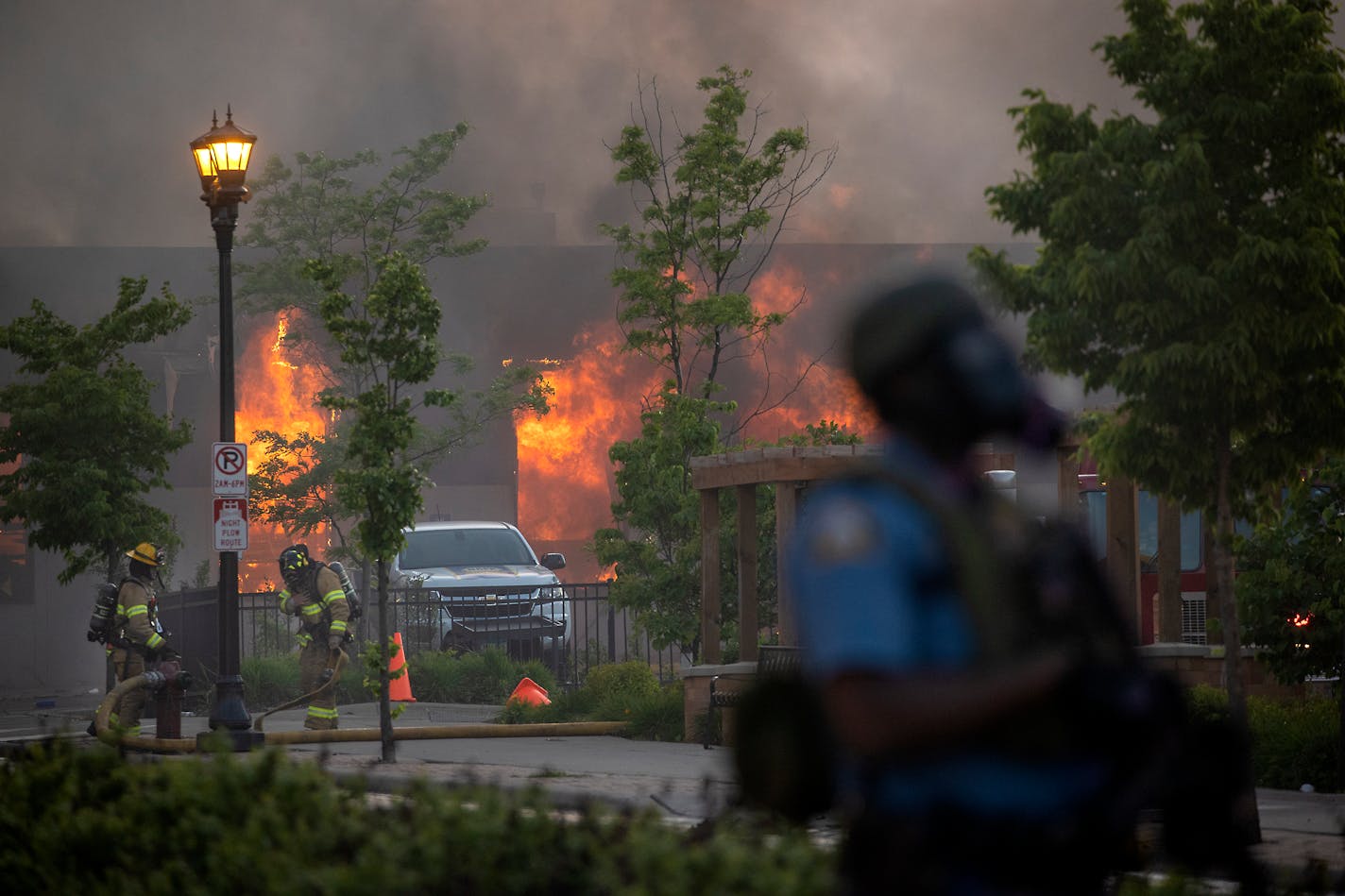 Firefighters battle flames at a business along University Avenue in St. Paul as riot officers police the street on May 28. Protests over the death of George Floyd, a Black man who died in police custody, had broken out in Minneapolis and St. Paul for a third straight night.