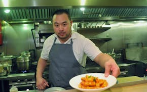Man in short-sleeved white shirt and gray apron hands dish over counter with restaurant kitchen in background.