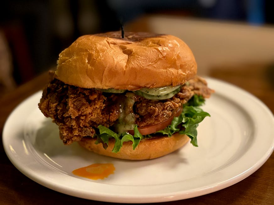 A thick, breaded chicken sandwich with chili crisp, topped with green lettuce on a toasted bun