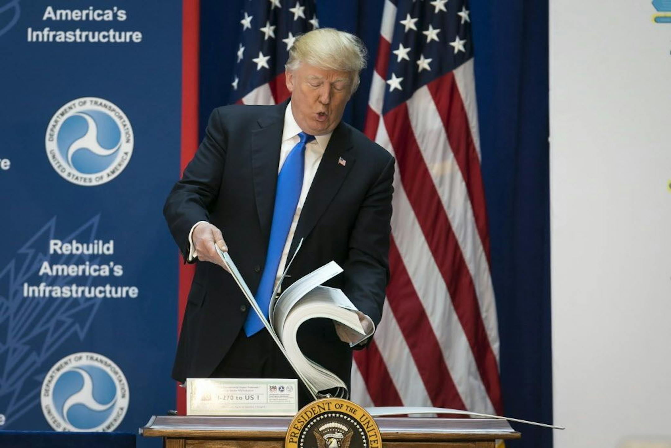 President Donald Trump shows the size of environmental impact road planning documents for a highway in Maryland while speaking about infrastructure plans at the Department of Transportation in Washington, June 9, 2017.