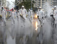 Taiwanese army soldiers wearing protective suits spray disinfectant over a road during a drill to prevent community cluster infection, in New Taipei C