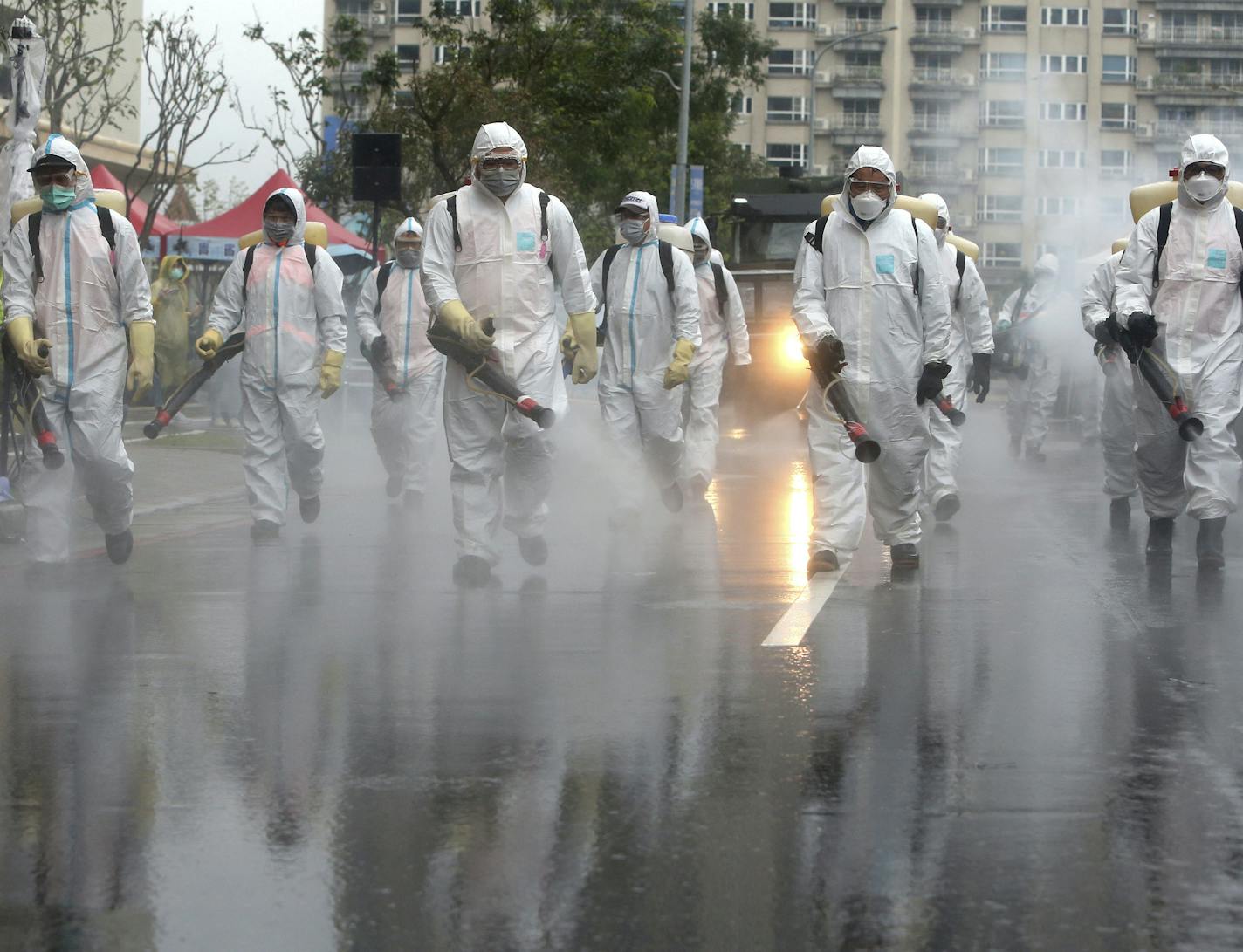 Taiwanese army soldiers wearing protective suits spray disinfectant over a road during a drill to prevent community cluster infection, in New Taipei City, Taiwan, Saturday, March 14, 2020. The city&#x2019;s authorities conducted the drill to simulate the situation before and after community cluster infection of the new coronavirus. The drill&#x2019;s scenario assumes that the COVID-19 had spread within a community of hundreds of people living in buildings. For most people, the new coronavirus ca