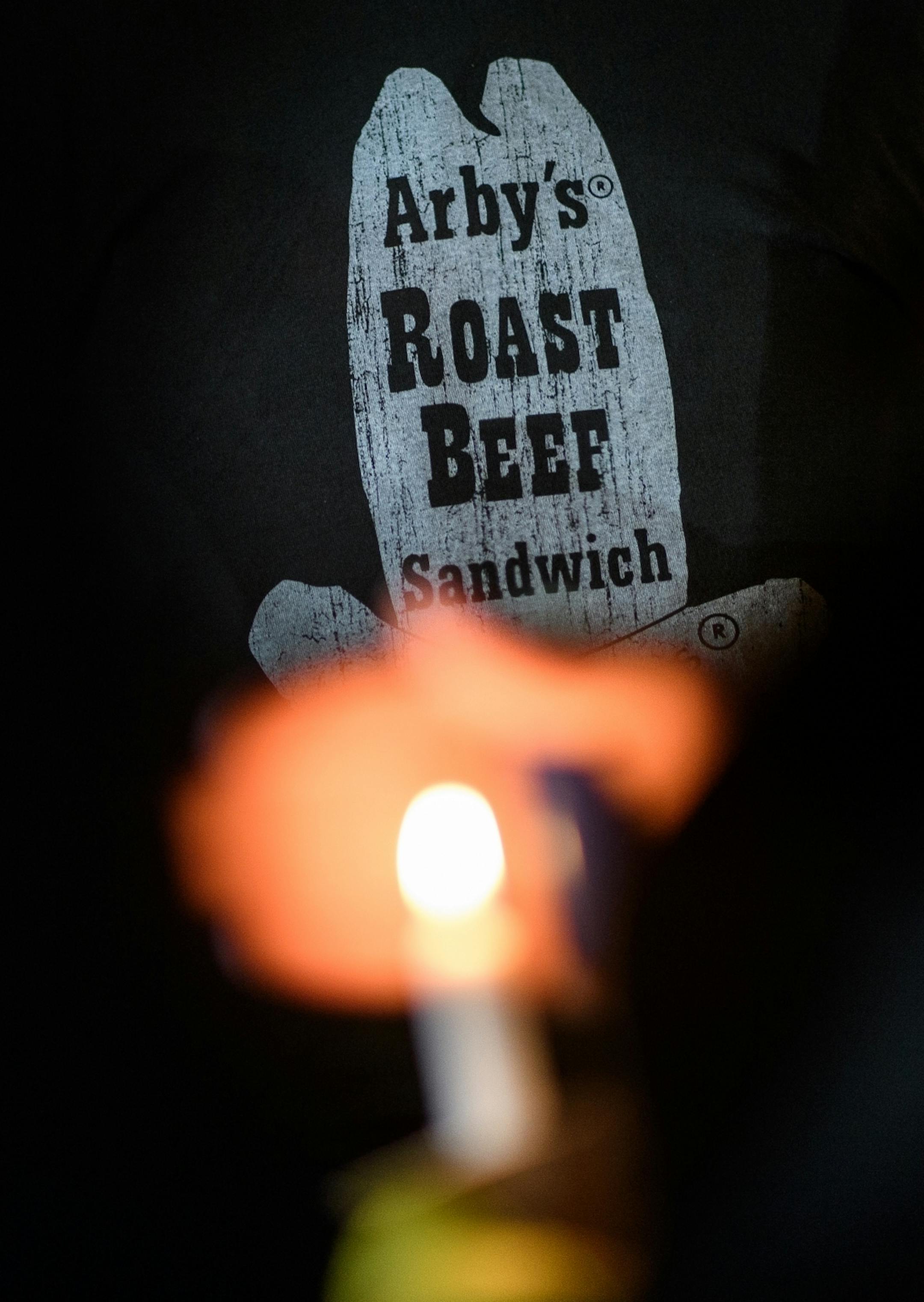 A vigil goer held a candle in front of a fellow mourner's Arby's t-shirt Friday night.