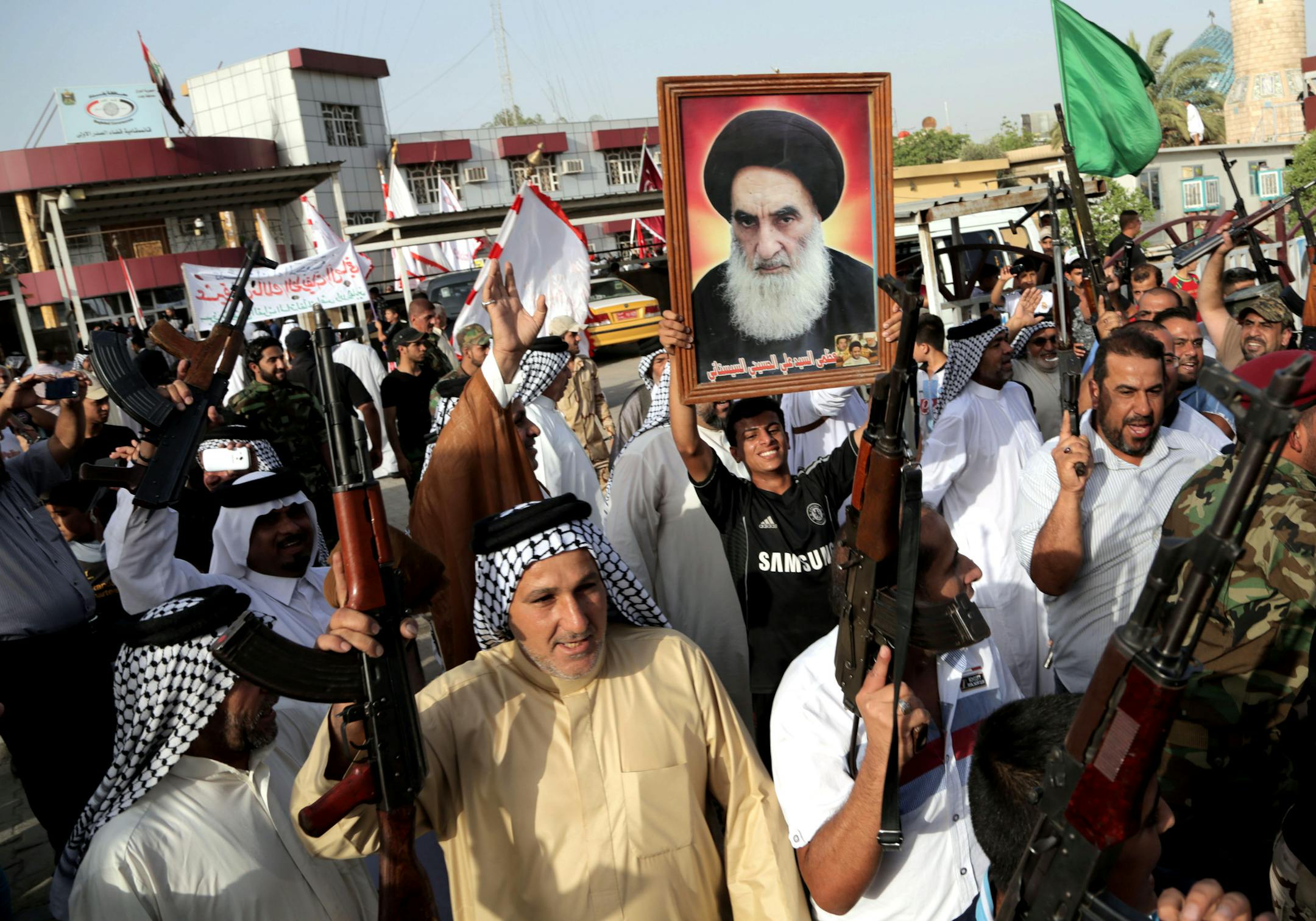 Iraqi Shiite tribal fighters raise their weapons and chant slogans against the Iraqi militants, in Baghdad's Sadr City, Iraq, Wednesday, June 18, 2014. The poster depicts Shiite spiritual leader Grand Ayatollah Ali al-Sistani.