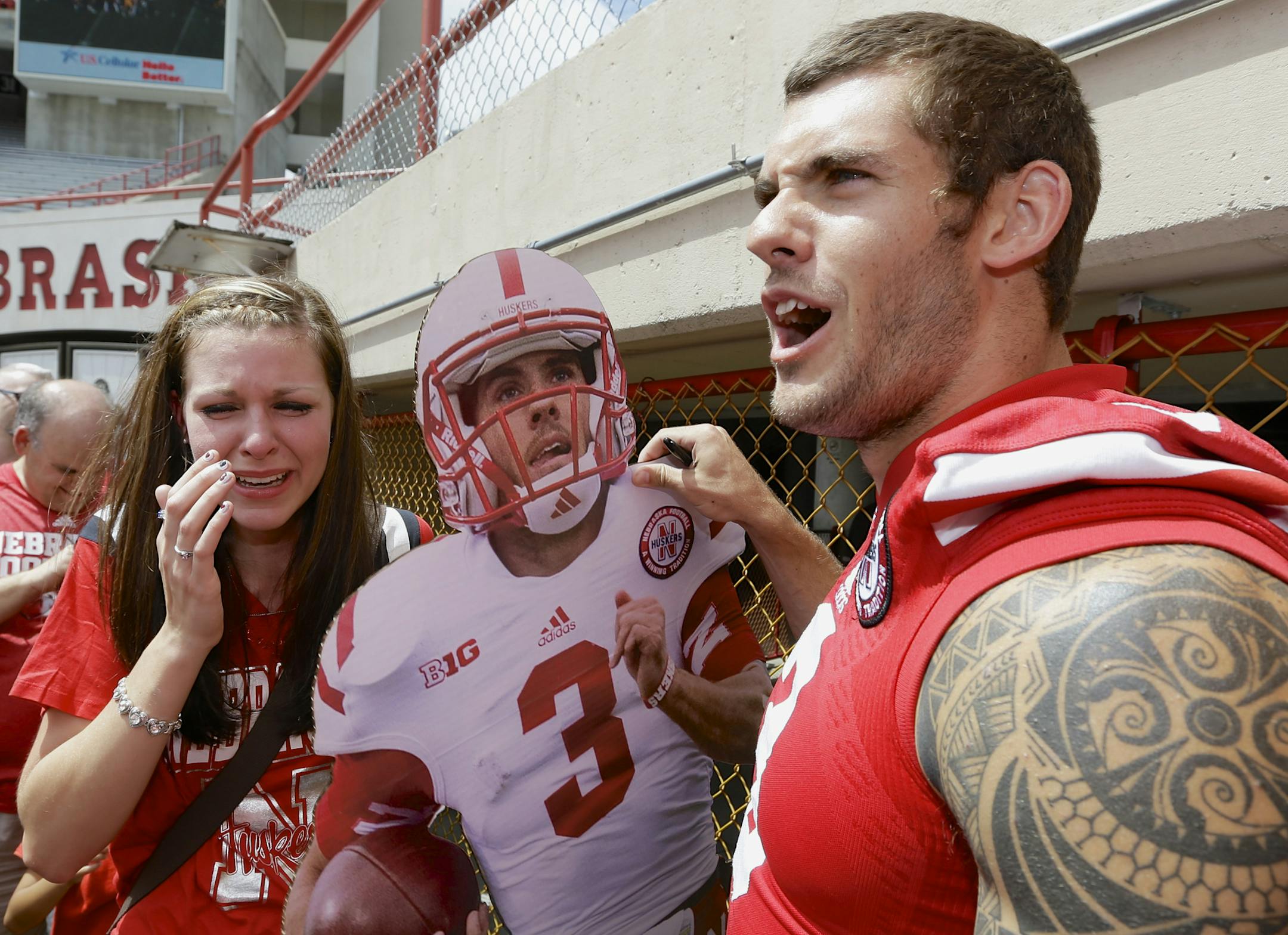 Nebraska fans strongly support Taylor Martinez. Joelle Freed, left, carrying a life-size cutout of Martinez, was overcome by emotion after meeting him during the annual fan day held at Memorial Stadium.