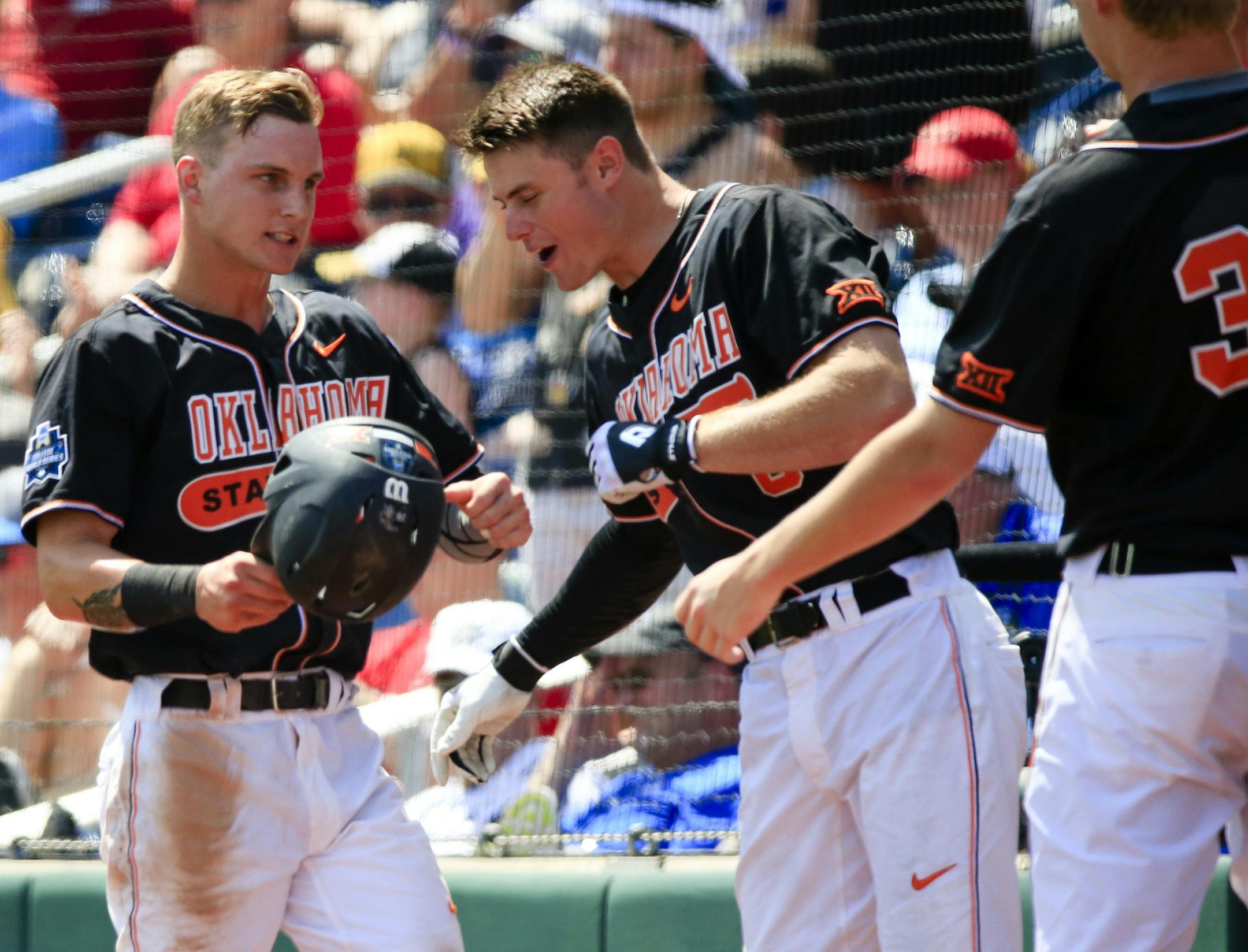 Oklahoma State's Corey Hassel, left, is greeted at the dugout by teammates after scoring against UC Santa Barbara on a single by Garrett Benge in the fourth inning of an NCAA men's College World Series baseball game in Omaha, Neb., Saturday, June 18, 2016. (AP Photo/Nati Harnik)