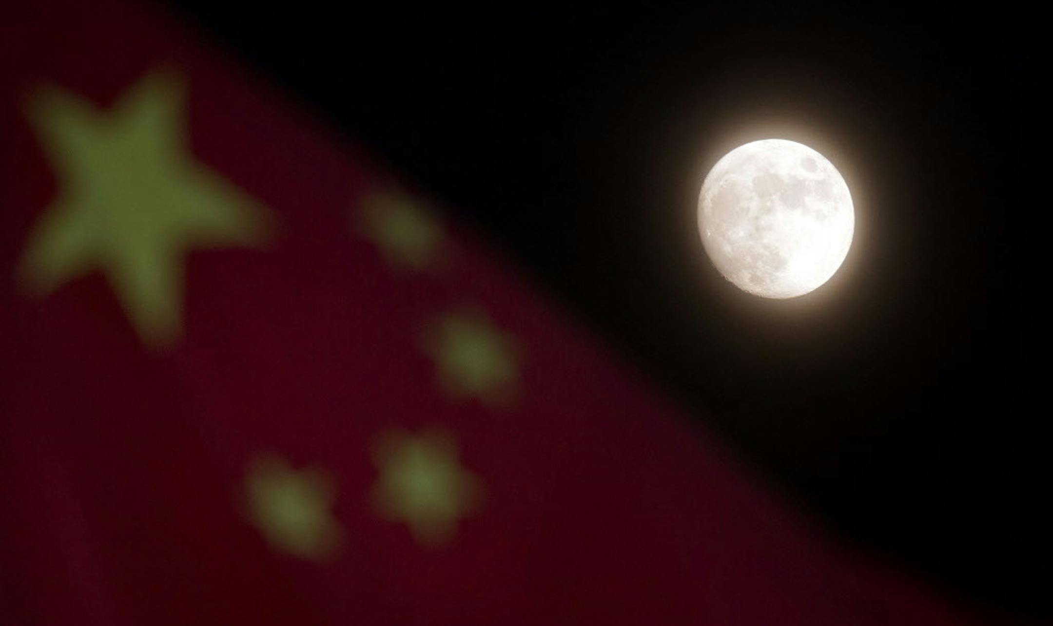 The moon is seen near a Chinese national flag in Beijing Sunday, Dec. 15, 2013. China's first moon rover touched the lunar surface and left deep traces on its loose soil, state media reported Sunday, several hours after the country successfully carried out the world's first soft landing of a space probe on the moon in nearly four decades. (AP Photo/Ng Han Guan)