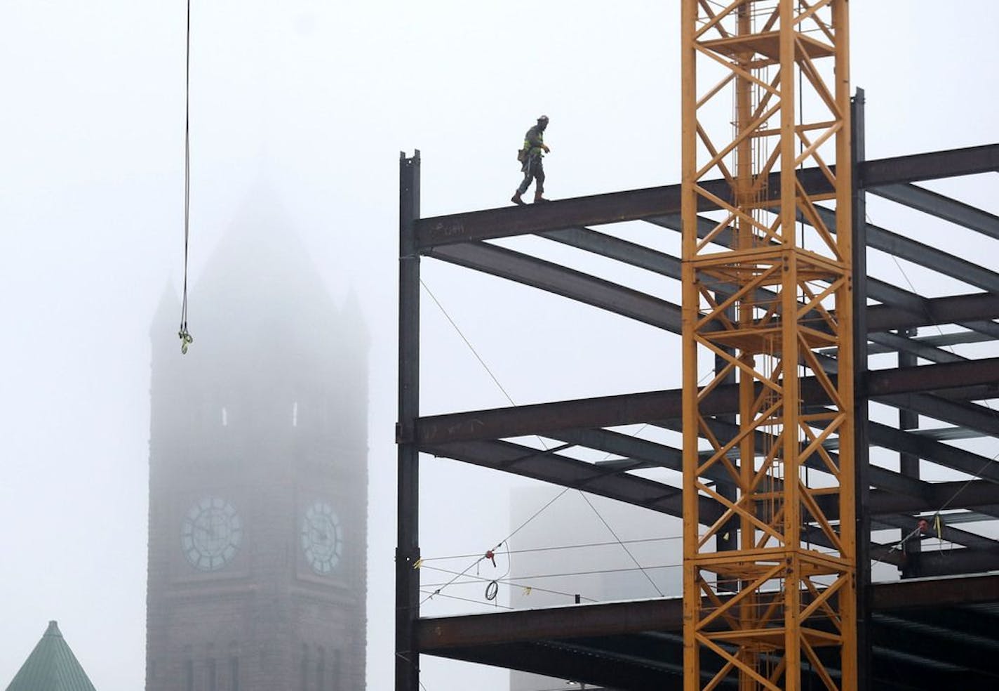 The Minneapolis City Hall Clock Tower is shrouded in fog and rain as a steel worker does his thing high up what will become the new Thrivent Corporate Center Wednesday, March 13, 2019, in downtown Minneapolis, MN.