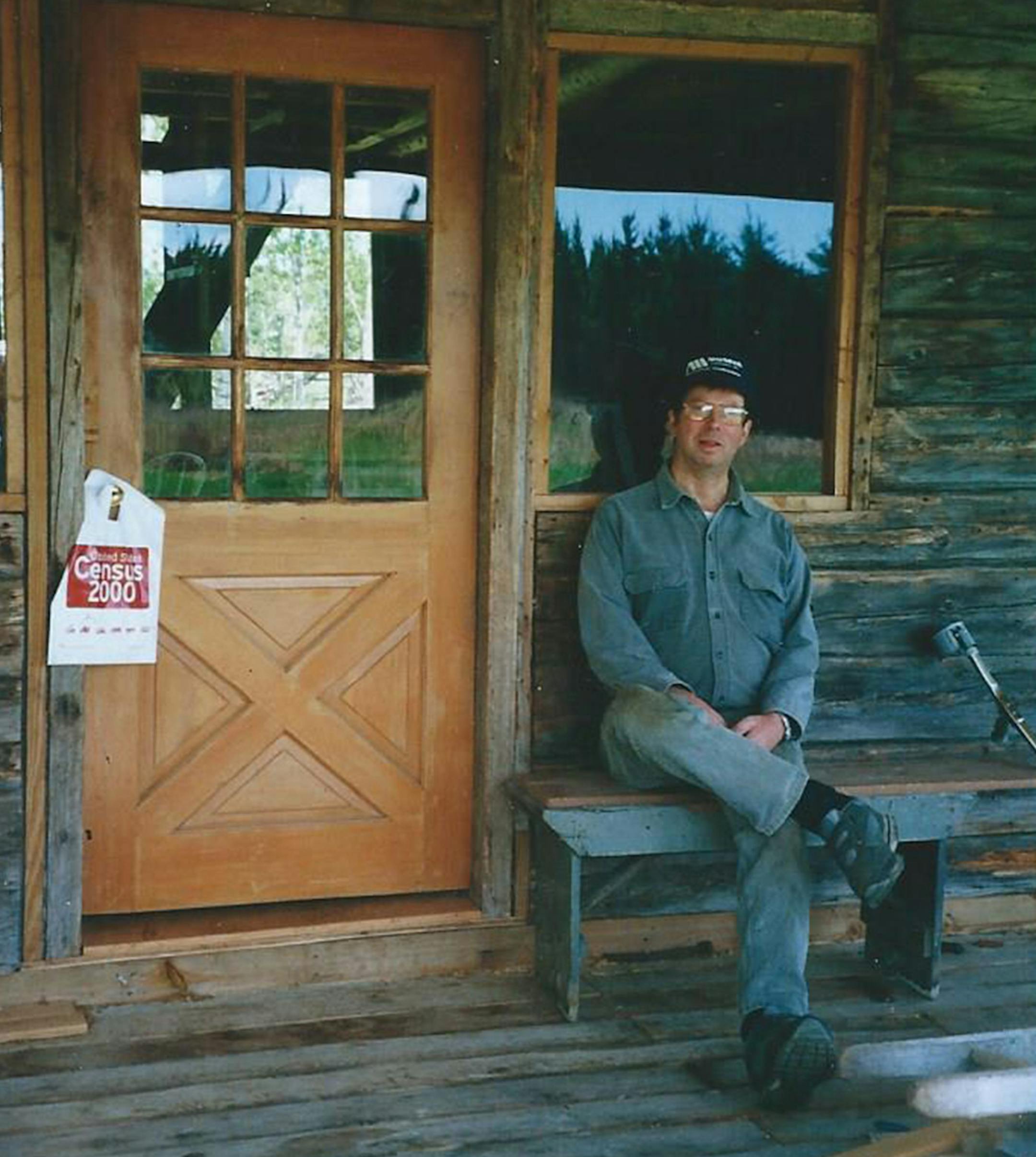 Gene Ullstrom sitting at cabin door in 2000. A Census envelop hung on the door.