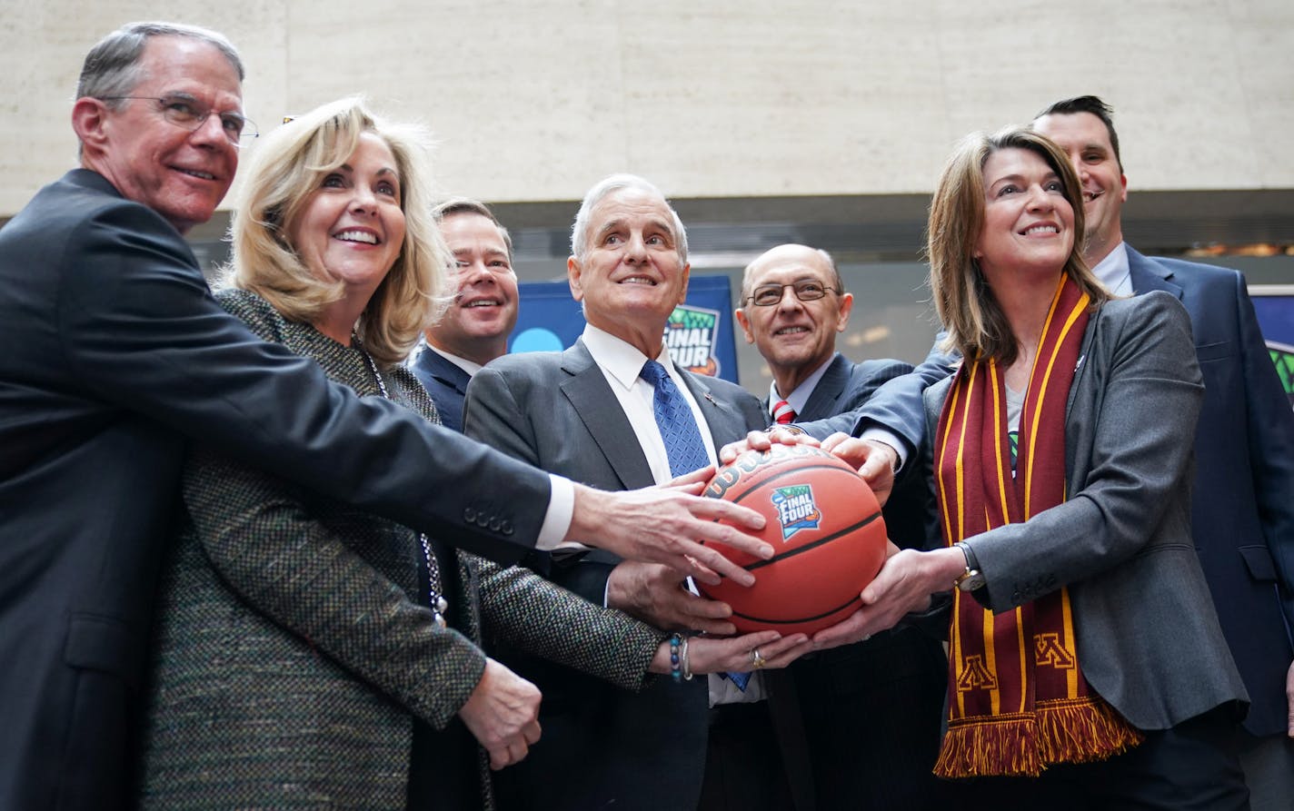 From left, local executives Richard Davis, Maureen Bausch, David Mortenson, Mike Vekich, Kate Mortenson, Tom McGinnis gathered around Gov. Mark Dayton to get their hands on the ceremonial ball for the handoff to next year's Final Four.