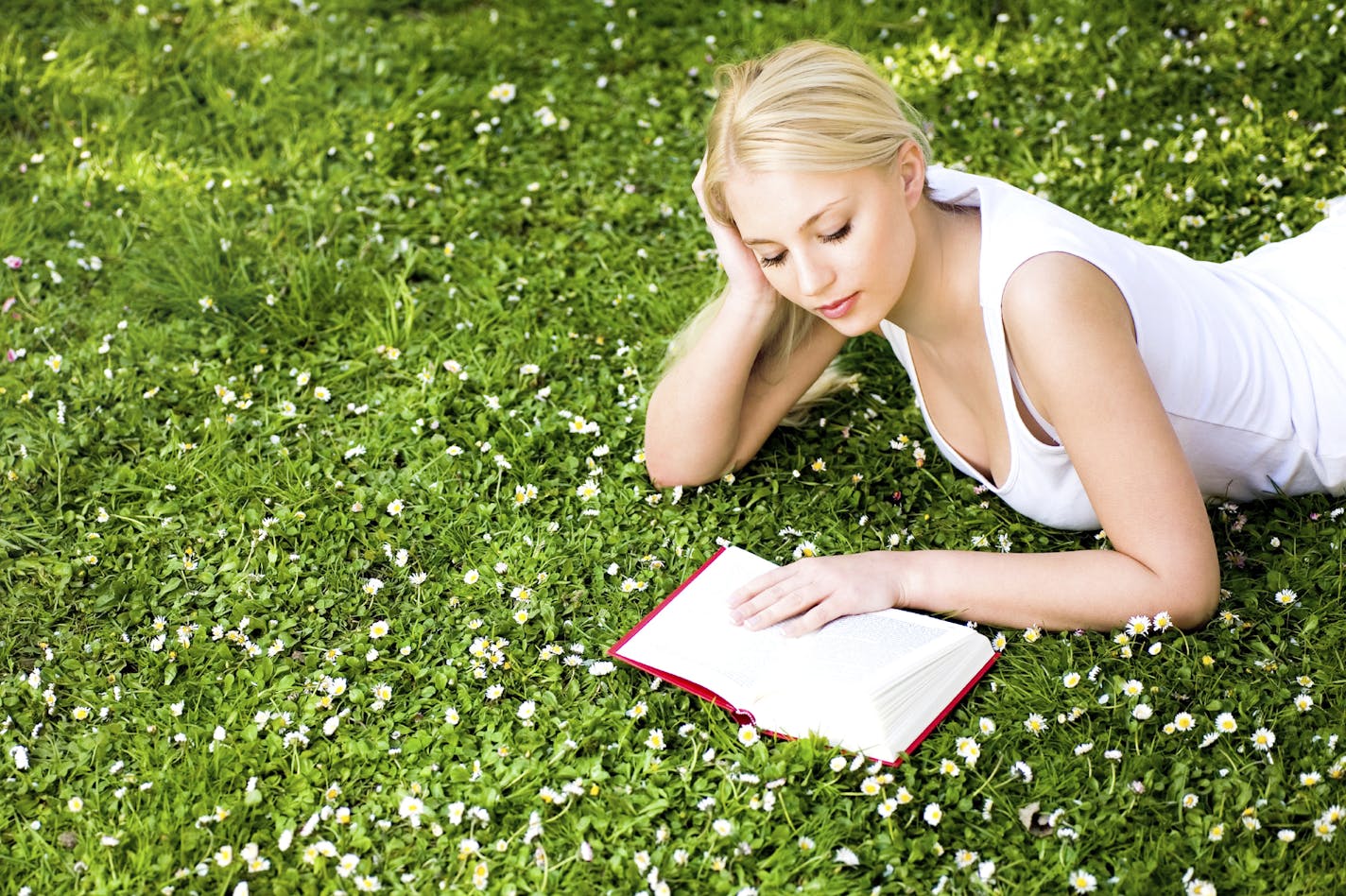 istock Woman on grass with flowers, reading book, white dress