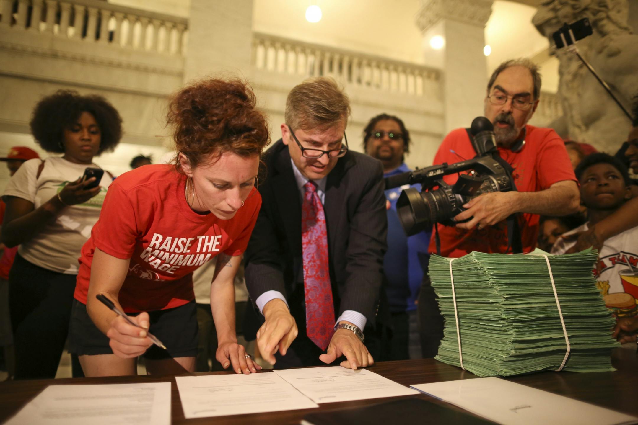 City Clerk Casey Carl showed Ginger Jentzen where to sign on the receipt for the stack of petitions with 20,000 signatures in support of a $15 minimum wage after demonstrators rallied in City Hall and heard speeches before handing over a petition with 20,000 signatures on it to the City Clerk.