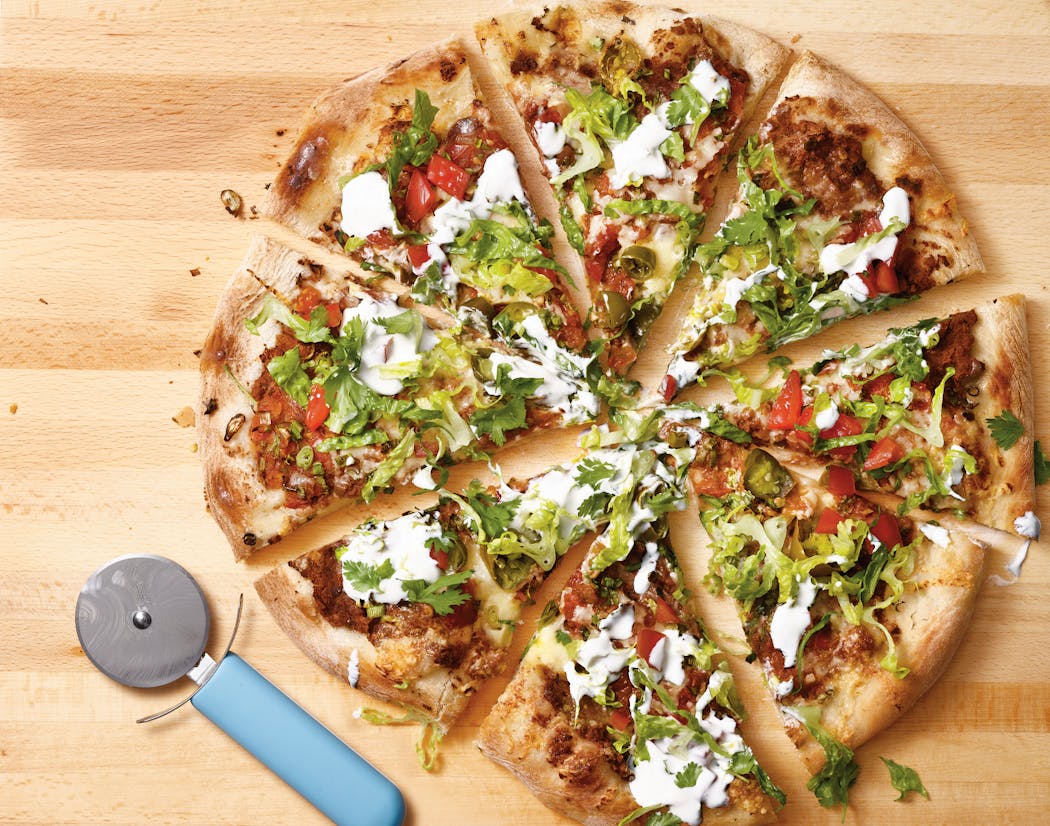 Taco pizza has a base of refried beans and is topped with salsa, cheese and other taco fixings.