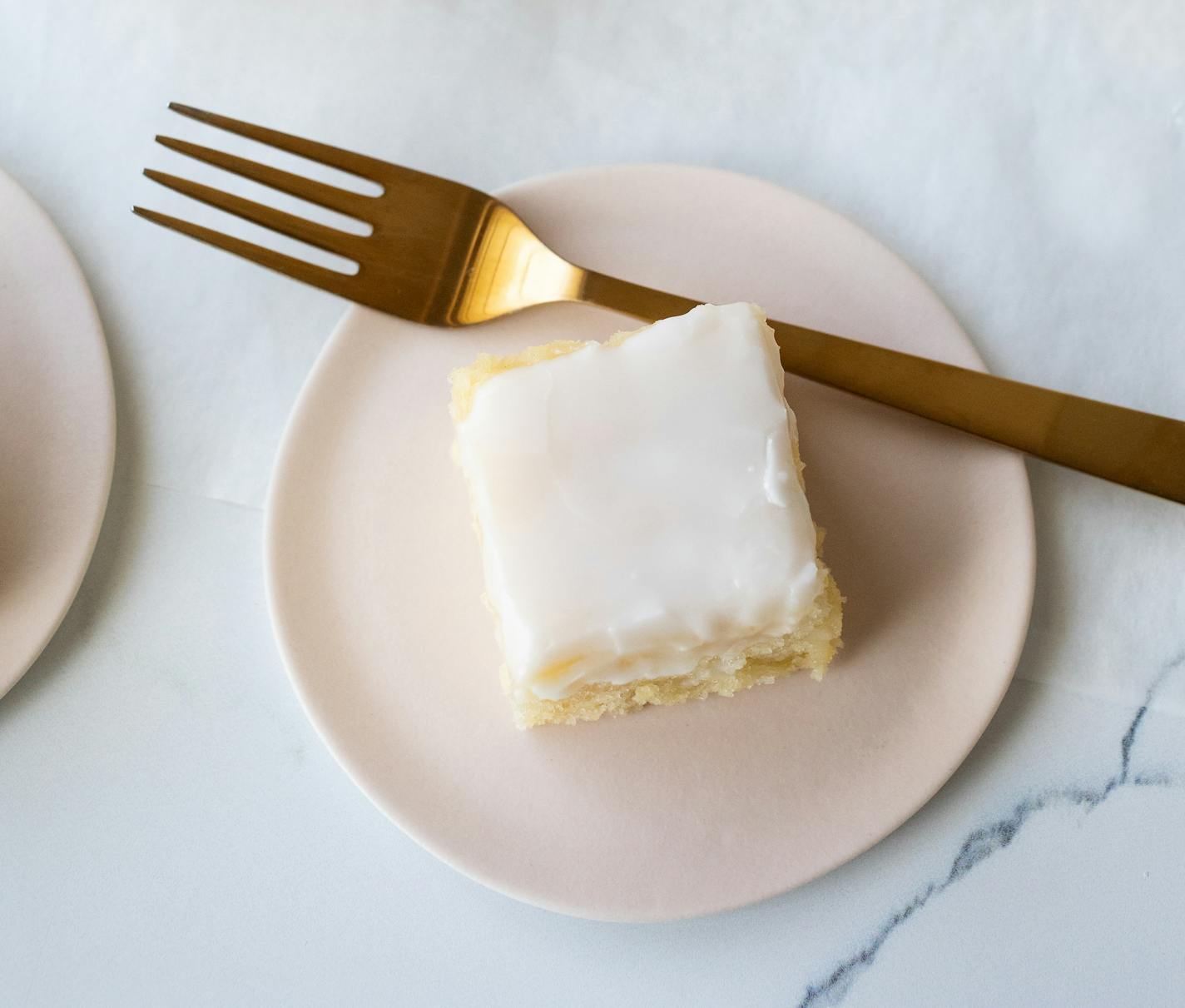 A plate with a slice of lemon snacking cake topped with a lemon glaze.