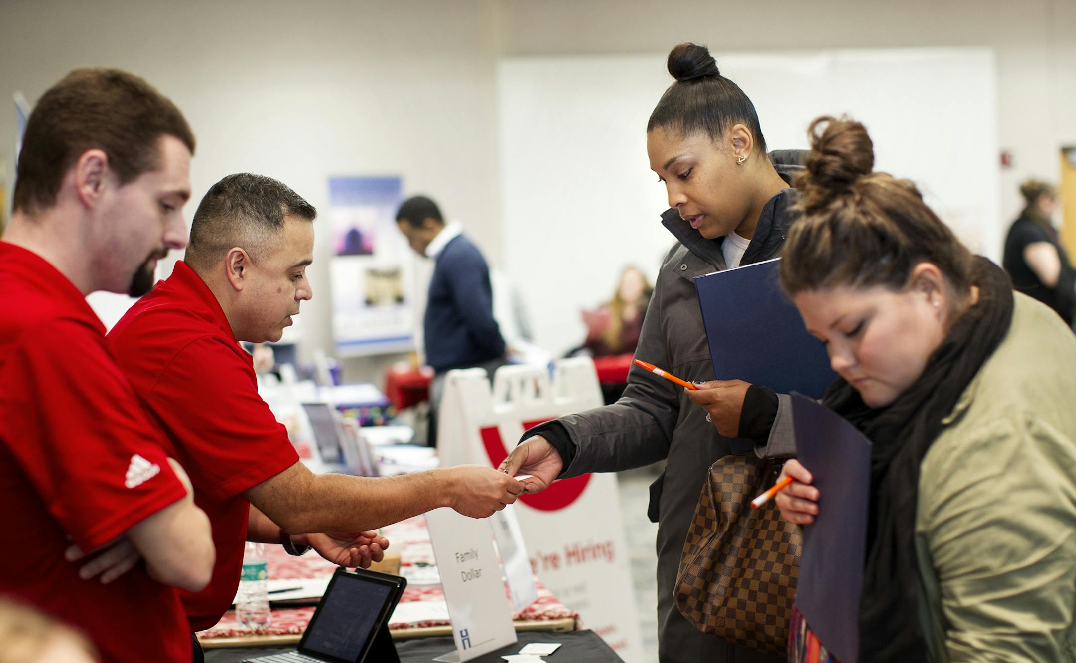 Ebony Johnson, second from right, and Lex Macaulay take business cards and information packets from hiring employers during a Job Development Career Fair at Brookdale Library in Brooklyn Center December 7, 2015. The two women work in recruiting for the nonprofit Rise and assist people in finding job opportunities. They attended the fair to gather information for their clients. (Courtney Perry/Special to the Star Tribune)