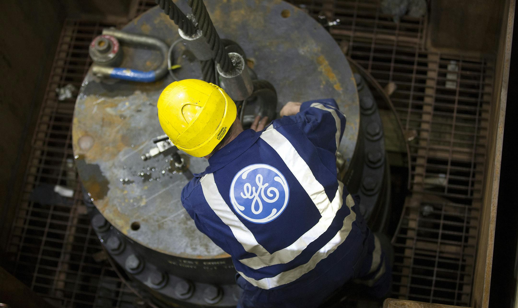 The company logo sits on an employee's overalls as he secures a metal cable to a section of a subsea oil and gas tree, at the General Electric Co. (GE) plant in Montrose, U.K., on Wednesday, Dec. 11, 2013. U.K. industrial production rose for a second month in October, a sign that the economic recovery maintained momentum at the start of the fourth quarter. Photographer: Simon Dawson/Bloomberg ORG XMIT: 456598053