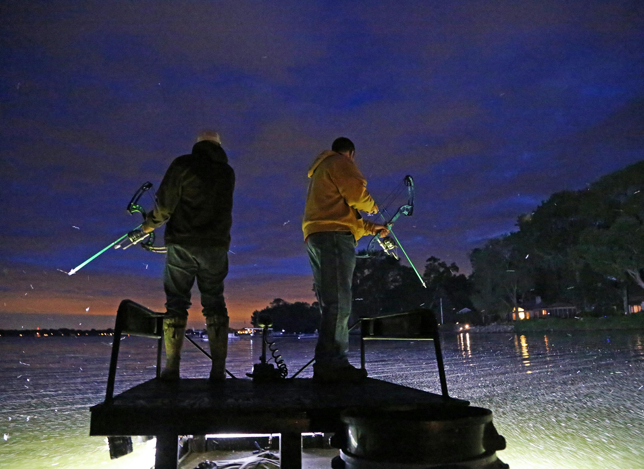 Amid a mayfly hatch, bowfishermen Vaghn Nelson, left, and Scott Stroyny, both of the Twin Cities area, patrol a metro lake Wednesday night, looking for carp.