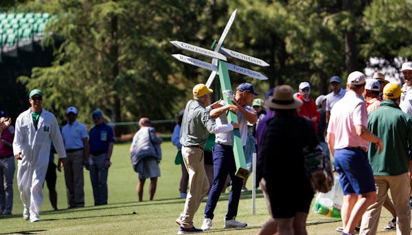Bryson DeChambeau, center, carries a Masters directions sign along the 13th fairway after hitting into the trees during round two of the Masters tourn