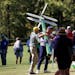 Bryson DeChambeau, center, carries a Masters directions sign along the 13th fairway after hitting into the trees during round two of the Masters tourn