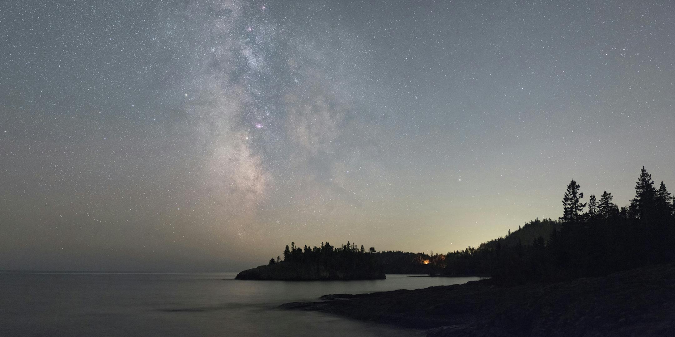 ONE TIME USE. Camping in Minnesota's state parks is a great way to observe the Milky Way and its night sky treasures. Their dark skies give you some of the best observing possibilities in the state. In this scene from Split Rock Lighthouse State Park, you can find the sparkling galactic core region of the Milky Way poised over Ellingson Island in Lake Superior, as well as a late night campfire glowing in the trees. See if you can find the four pinkish objects arranged vertically along the middle