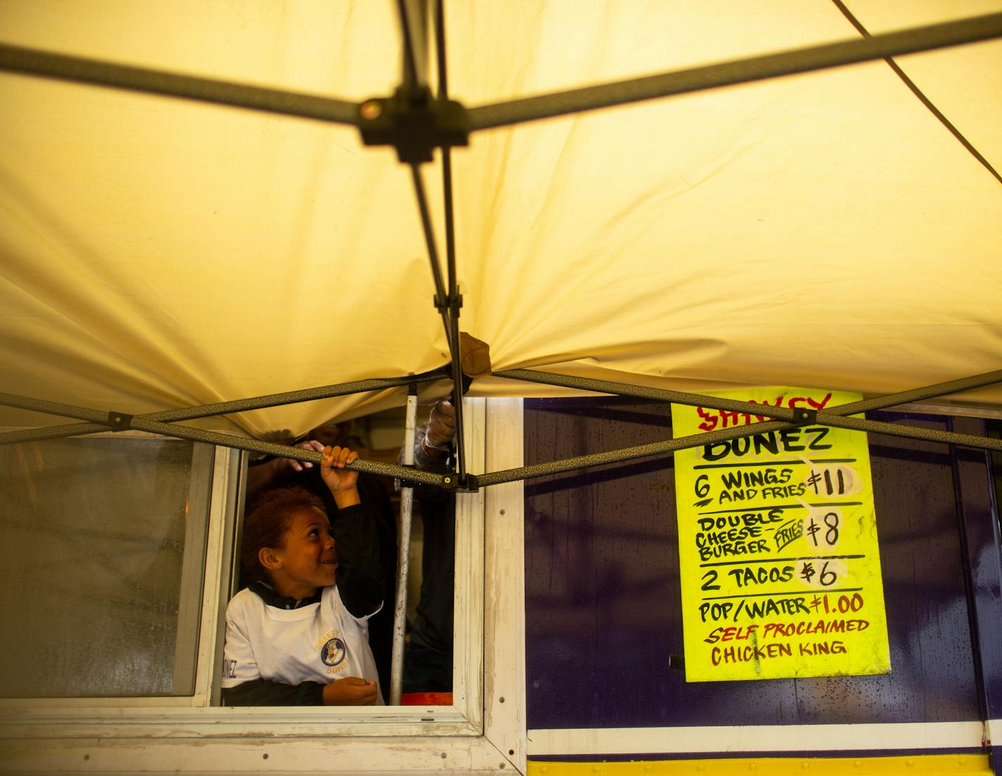 Durall Chappell, 6, helps hold down the tent in front of the Shakey Bonez food truck as the wind picks up Saturday at St. Paul's Rondo Days festival.