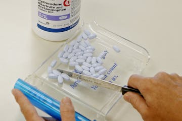 FILE - In this Aug. 5, 2010 file photo, a pharmacy tech poses for a picture with hydrocodone bitartrate and acetaminophen tablets, the generic version