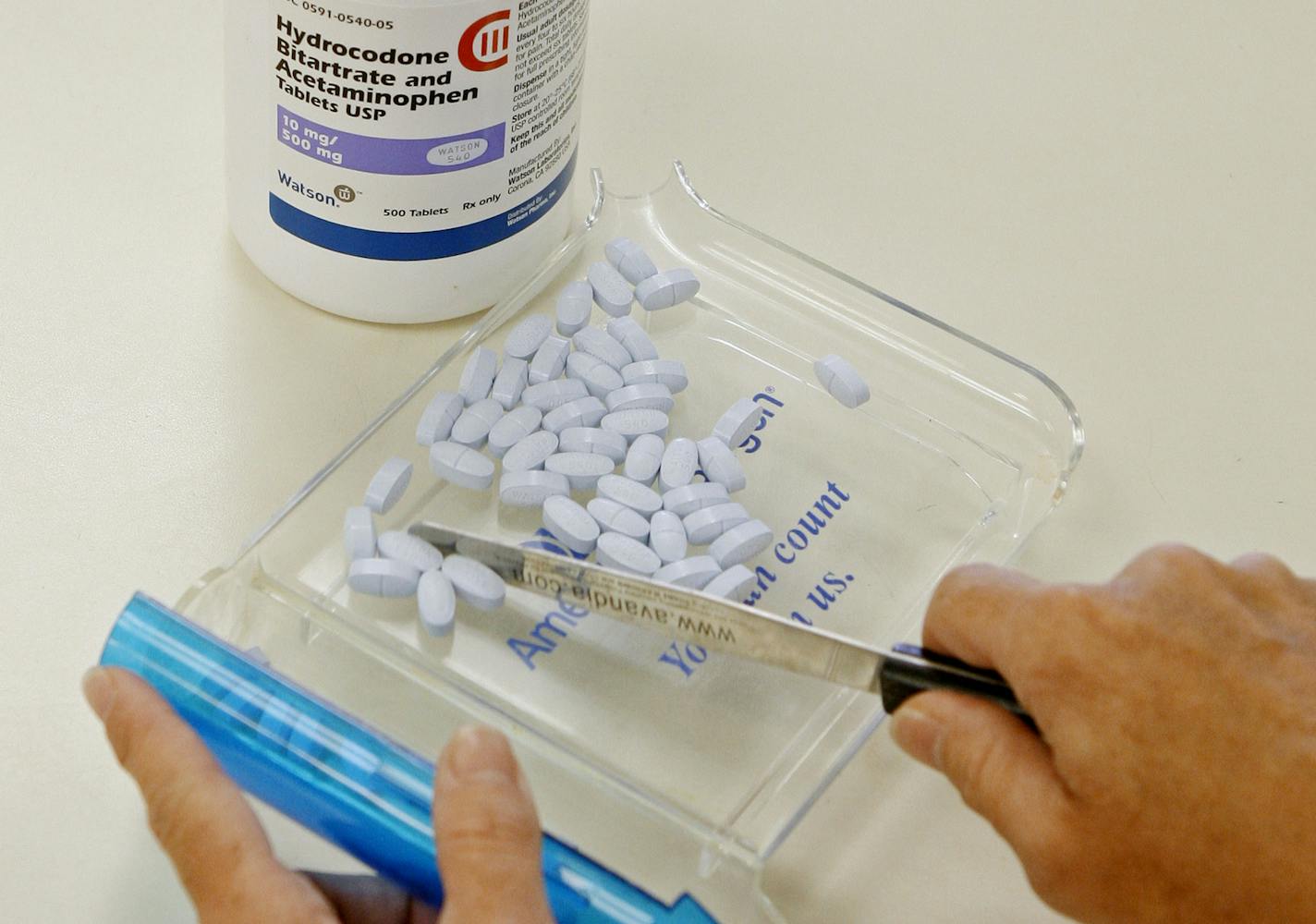 FILE - In this Aug. 5, 2010 file photo, a pharmacy tech poses for a picture with hydrocodone bitartrate and acetaminophen tablets, the generic version of Vicodin in Edmond, Okla. A report released Wednesday, May 31, 2017 traces how a short letter in a medical journal in 1980 helped sow the seeds of today's opioid epidemic by helping to convince doctors that these powerful painkillers carried less risk of addiction than they actually do. (AP Photo/Sue Ogrocki, File)