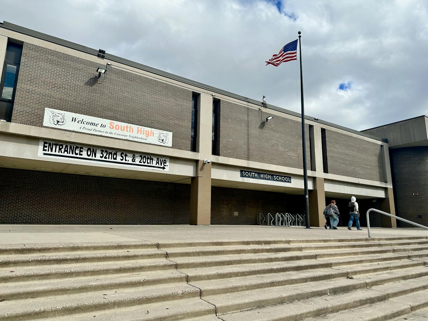 An American flag flies above a brutalist architecture-style building beneath a cloudy sky.